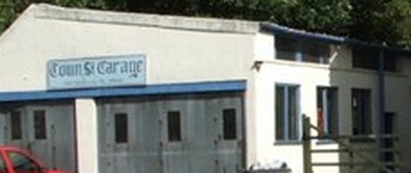 The workshop at 61 Town Street: a single-storey rendered building with a blue fascia, roller shutter doors and a painted sign reading Town St Garage.
